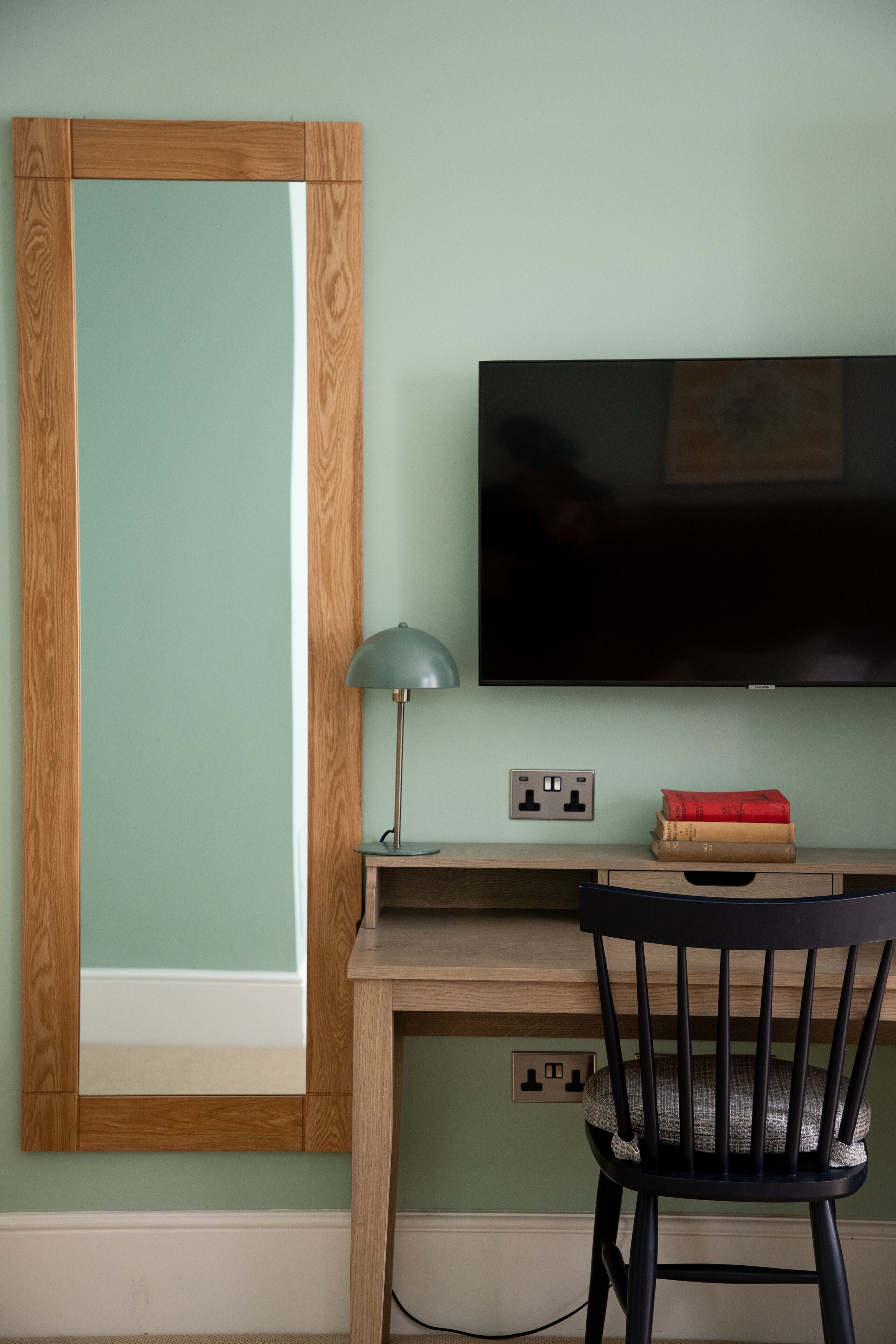 A room with a wooden desk, a black chair, a television, and a lamp.