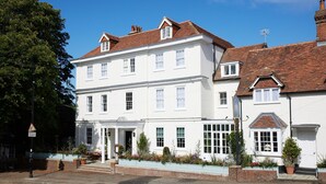 A two-story white building with a traditional design, featuring a front entrance with steps, a small porch, and a brick wall with potted plants. - The Georgian, Haslemere, Surrey (Haslemere)