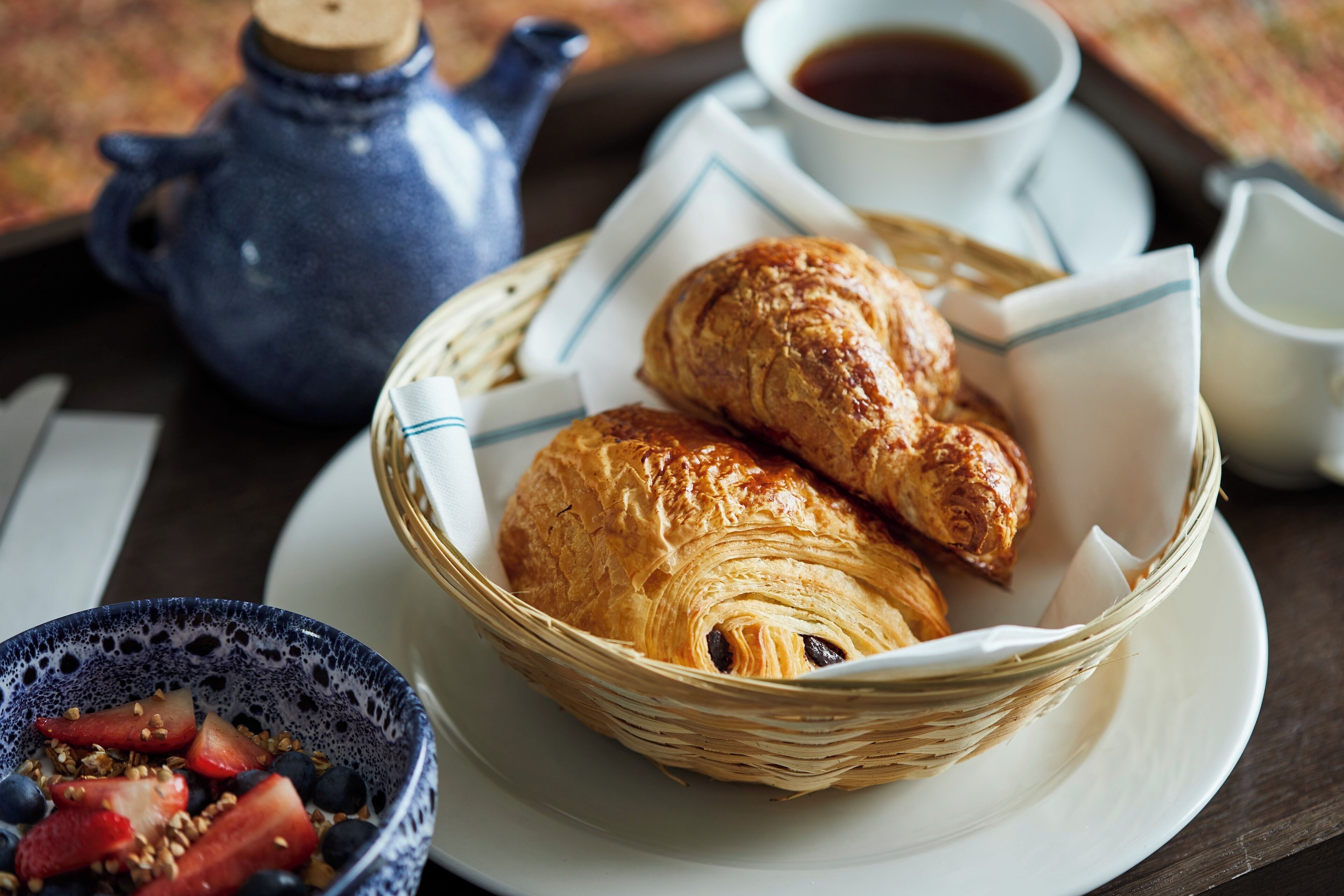 A breakfast setting with croissants, a bowl of fruit, and a teapot.