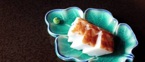 A green ceramic dish with a scalloped edge containing a white and brown food item, possibly a fish or meat, and a small green garnish.