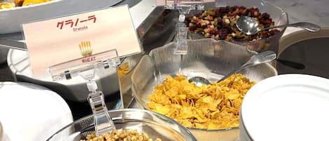 A buffet with various food options including granola, cornflakes, and cereal.