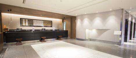 A modern hotel lobby with a marble floor, a reception desk, and a large wall-mounted artwork.