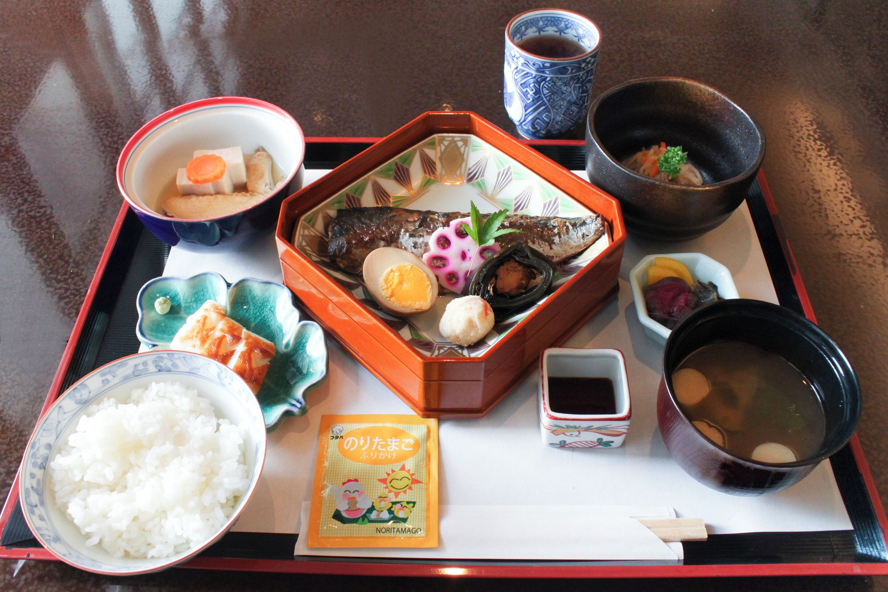Ein Tablett mit verschiedenen japanischen Speisen, darunter Reis, Fisch, Ei und Suppe.