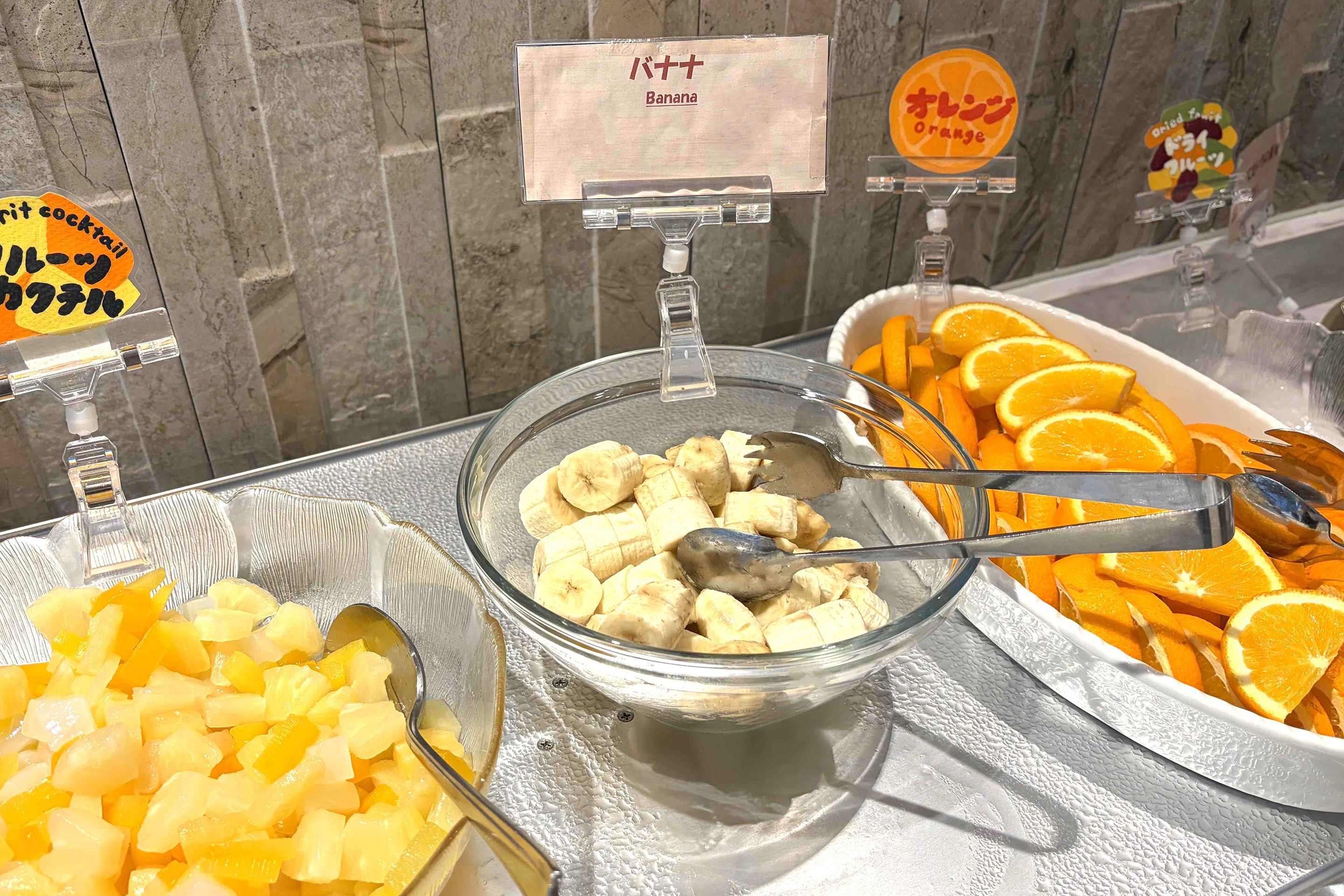 A buffet with various fruits including bananas, oranges, and pineapple chunks.