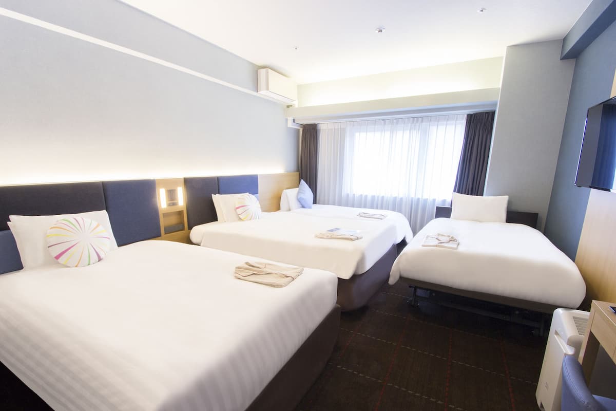 Une chambre d’hôtel avec trois lits simples, une télévision et une fenêtre avec des rideaux.