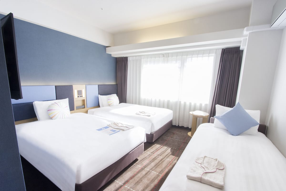 Une chambre d’hôtel avec deux lits, une télévision, une fenêtre avec des rideaux et une petite table.