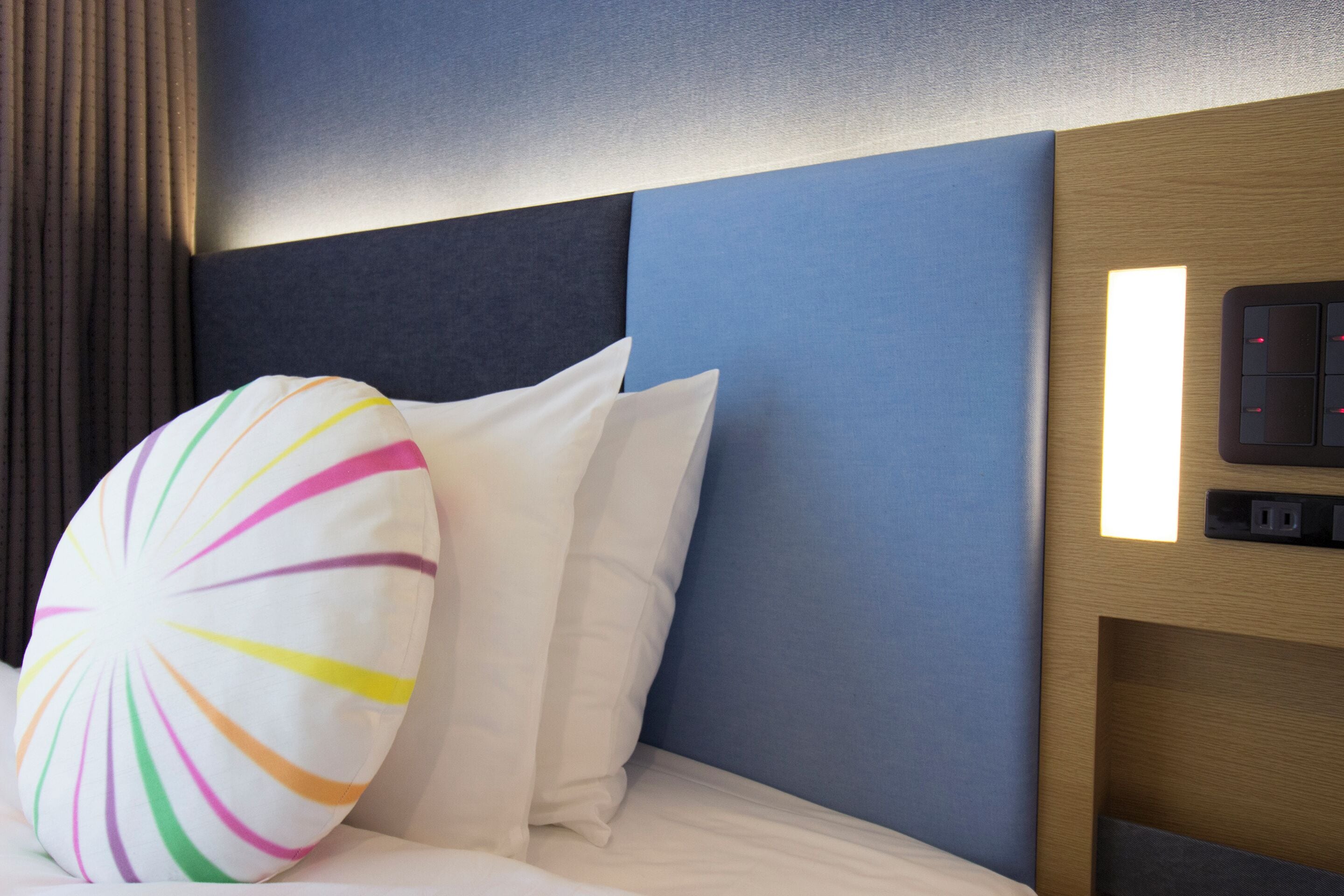 A hotel room with a bed, a headboard, and a wall-mounted control panel.
