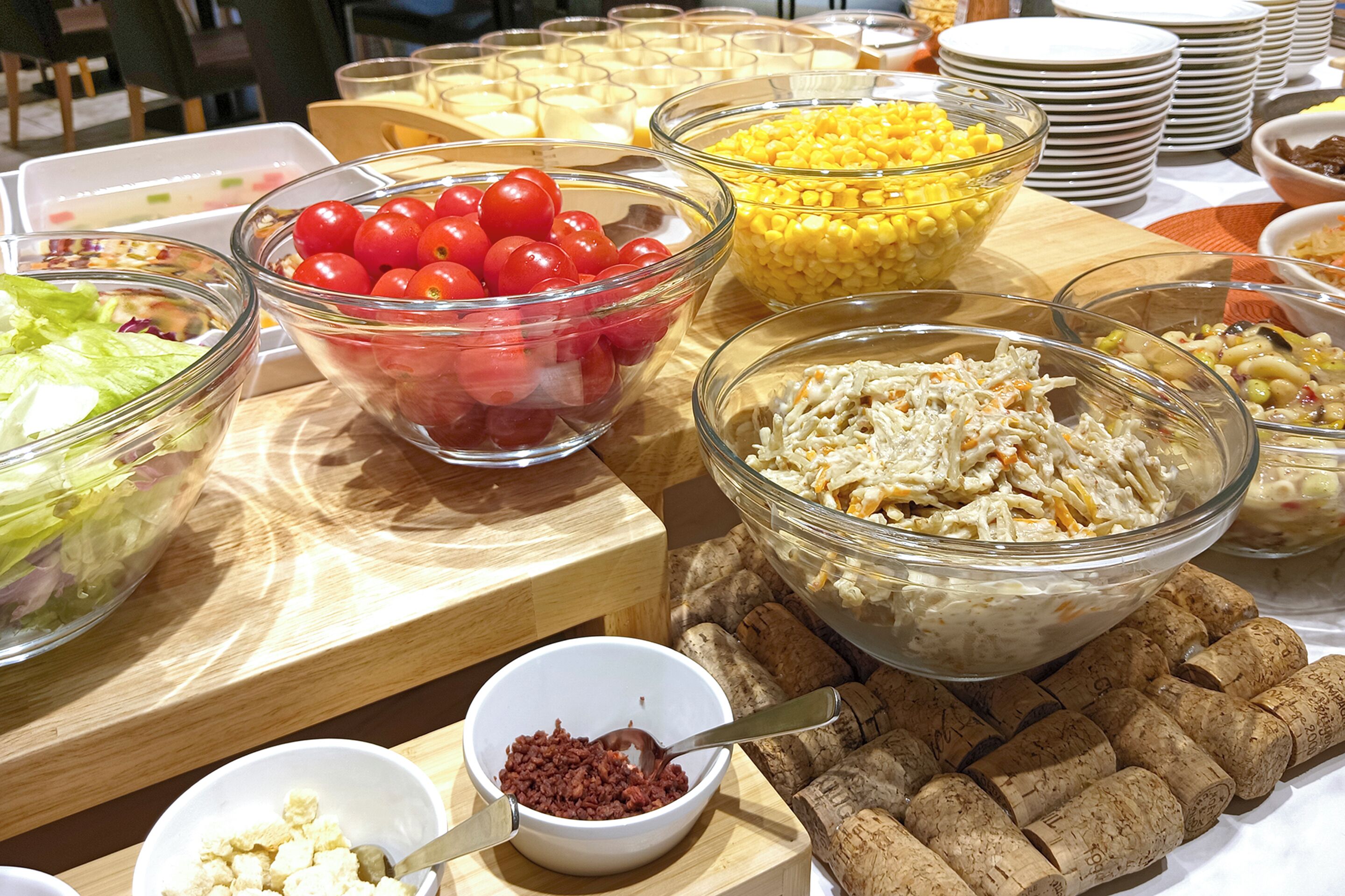 A buffet table with various food items including salads, tomatoes, corn, and pasta.