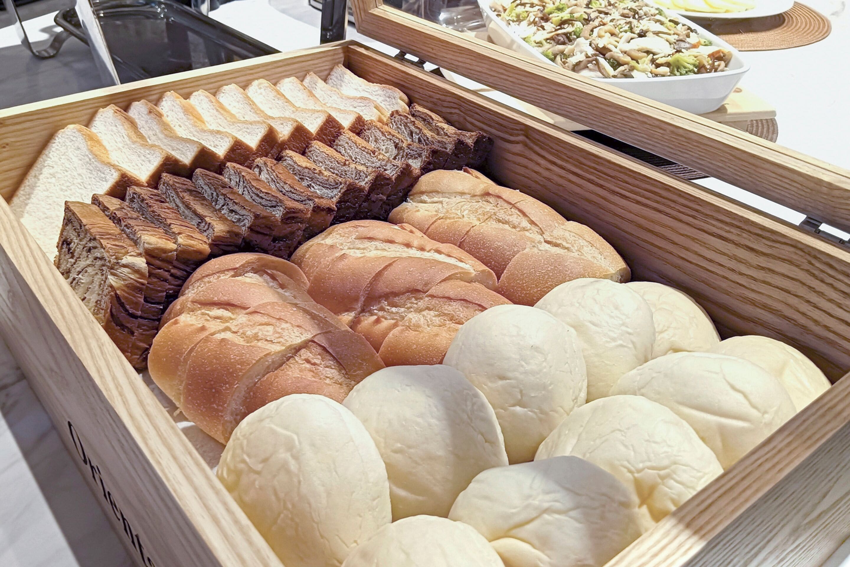 A wooden box containing various types of bread, including sliced bread and round loaves.
