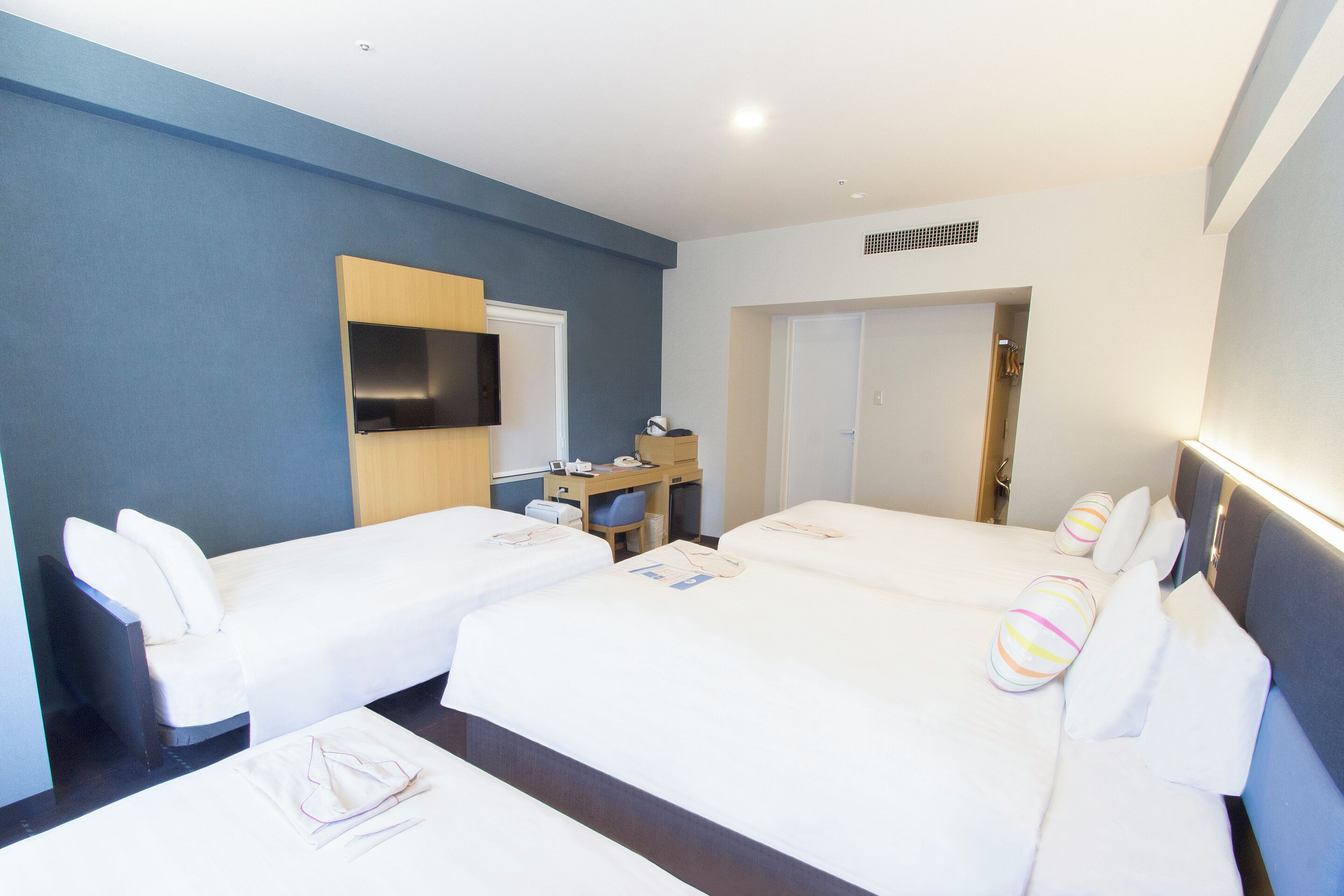 A hotel room with two beds, a desk, a mirror, and a wardrobe.