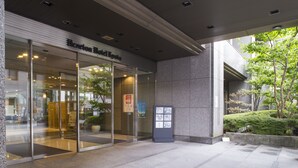 A hotel entrance with glass doors, a reception desk inside, and a small outdoor seating area with plants.