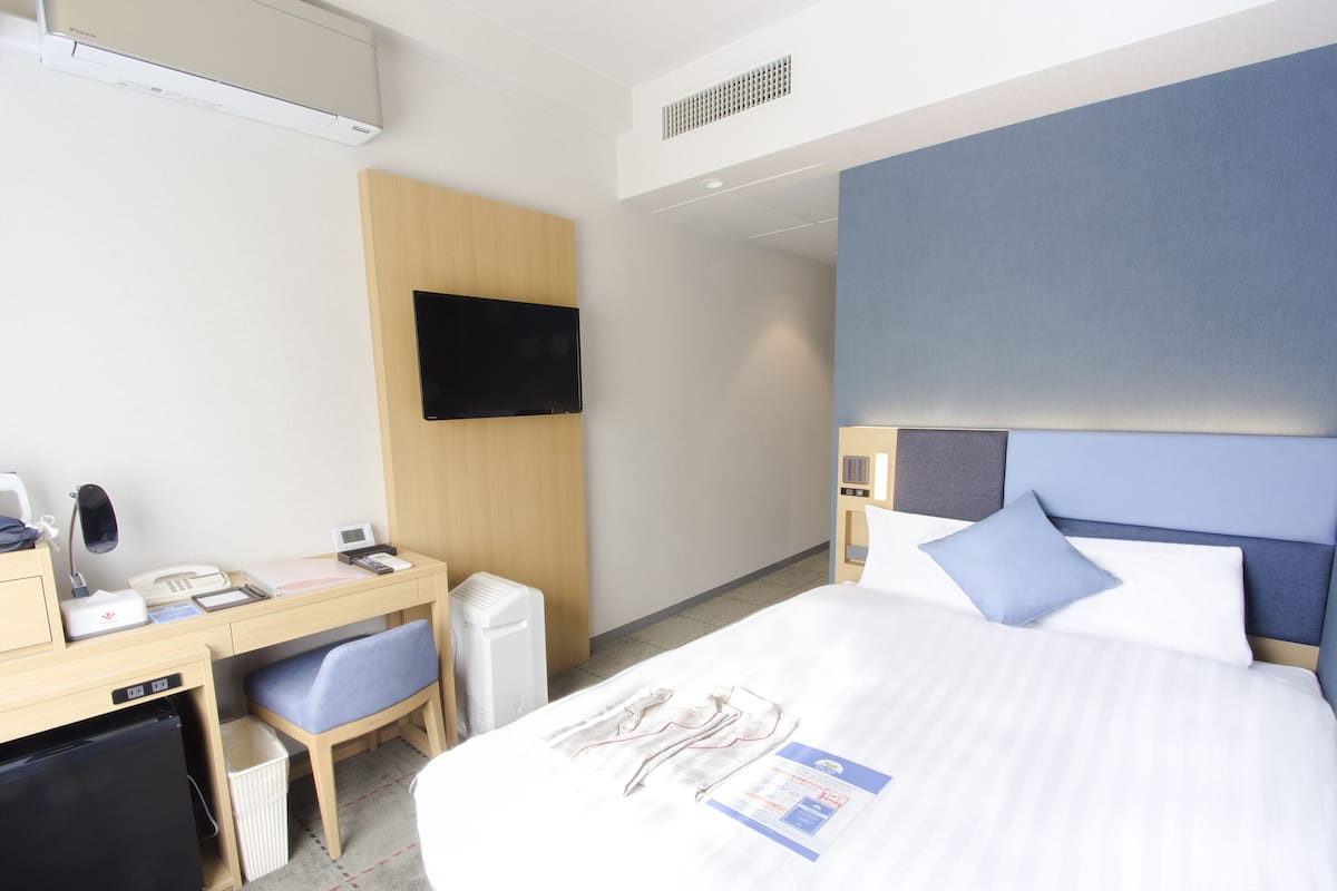 Une chambre d’hôtel comprenant un lit, un bureau avec une chaise, une télévision et une petite kitchenette.