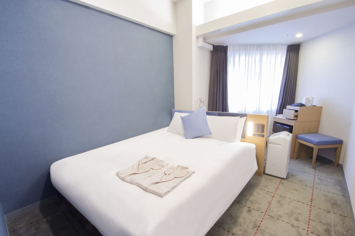 Une chambre d’hôtel avec un lit bien fait, un bureau avec une chaise et un petit coin salon.