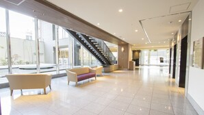 A spacious lobby with a staircase, seating area, and large windows.