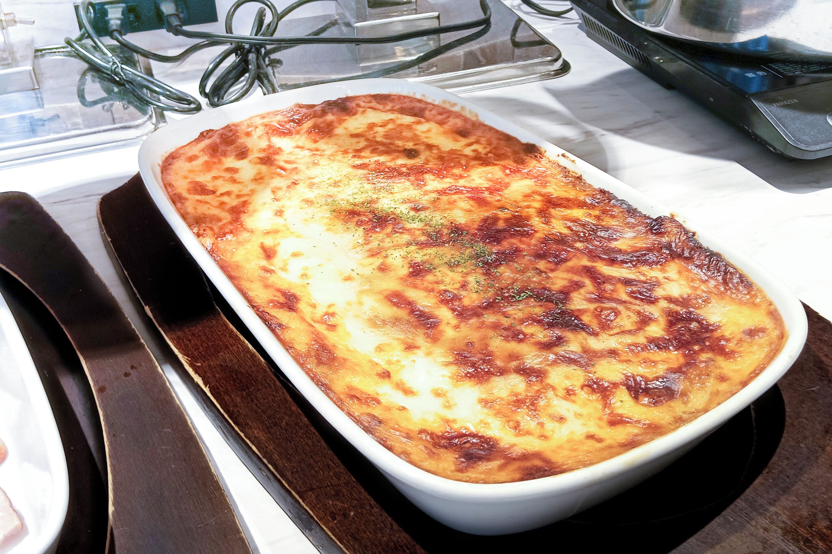 A rectangular white dish with a golden-brown top, placed on a dark tray.