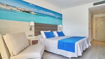 Een hotelkamer met een bed, een stoel, een nachtkastje en een schilderij van een strandgezicht.