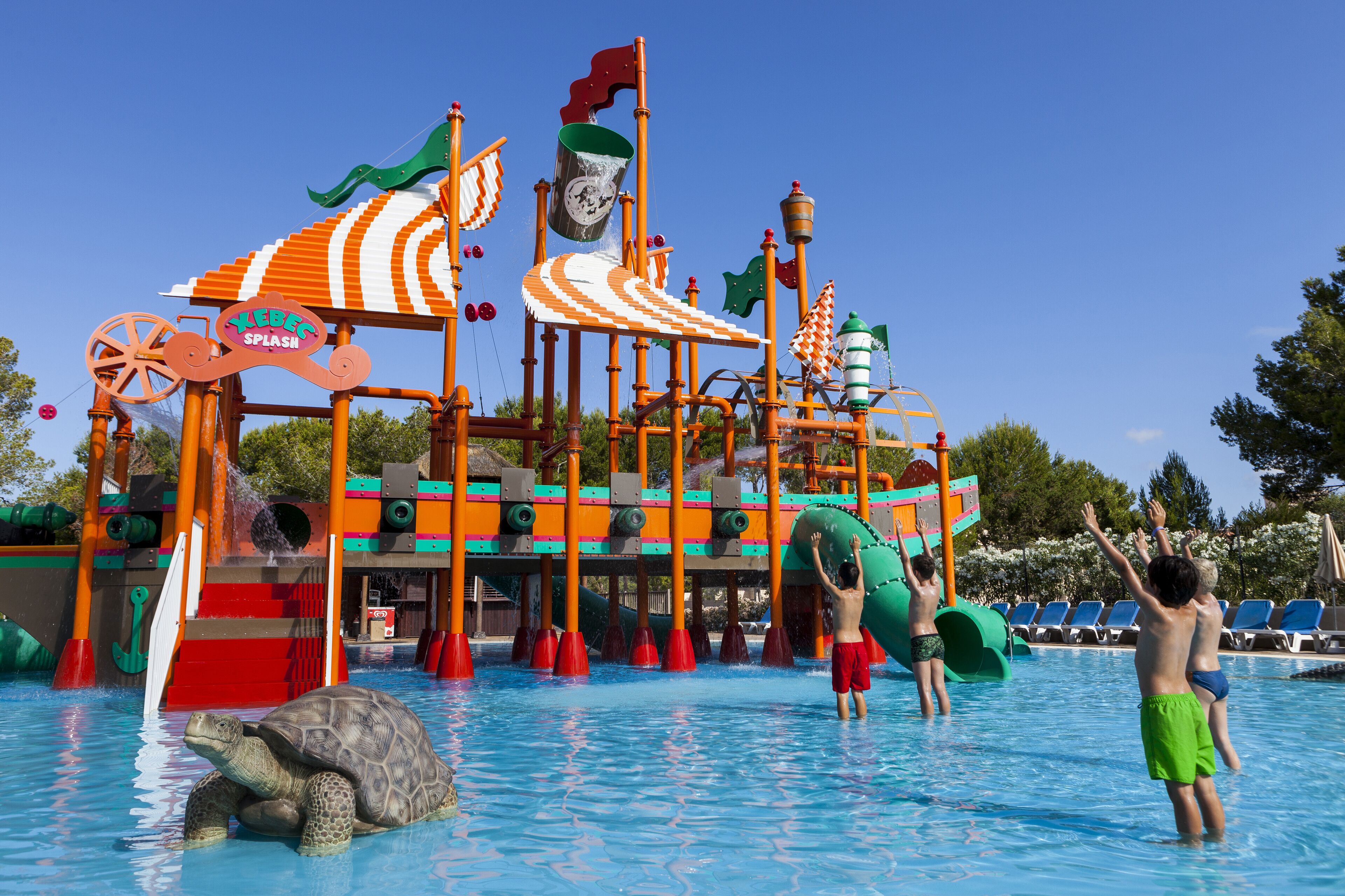 Un parque acuático con un tobogán gigante, una tortuga en la piscina y niños jugando.