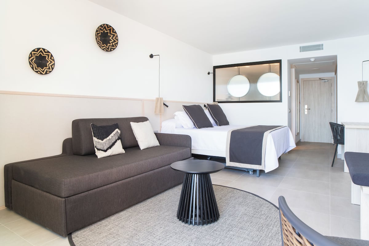 A modern hotel room with a sofa, a bed, a round table, and a mirror.