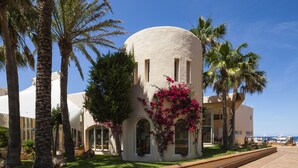 A building with a curved facade, arched windows, and a palm tree in the foreground. - Invisa Hotel Club Cala Verde (Santa Eulalia del Rio)
