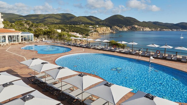 A swimming pool with sun loungers and umbrellas, a beach, and mountains in the background. - Invisa Hotel Club Cala Verde (Santa Eulalia del Rio)