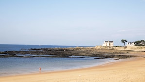 Une plage où l’on voit une personne se promener, un bâtiment sur le rivage et un ciel dégagé.