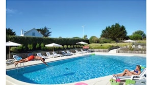 Une piscine entourée d’une haie et d’arbres, avec des chaises longues et des parasols.