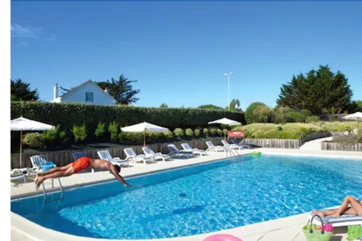 A swimming pool with lounge chairs and umbrellas, surrounded by a hedge and trees.