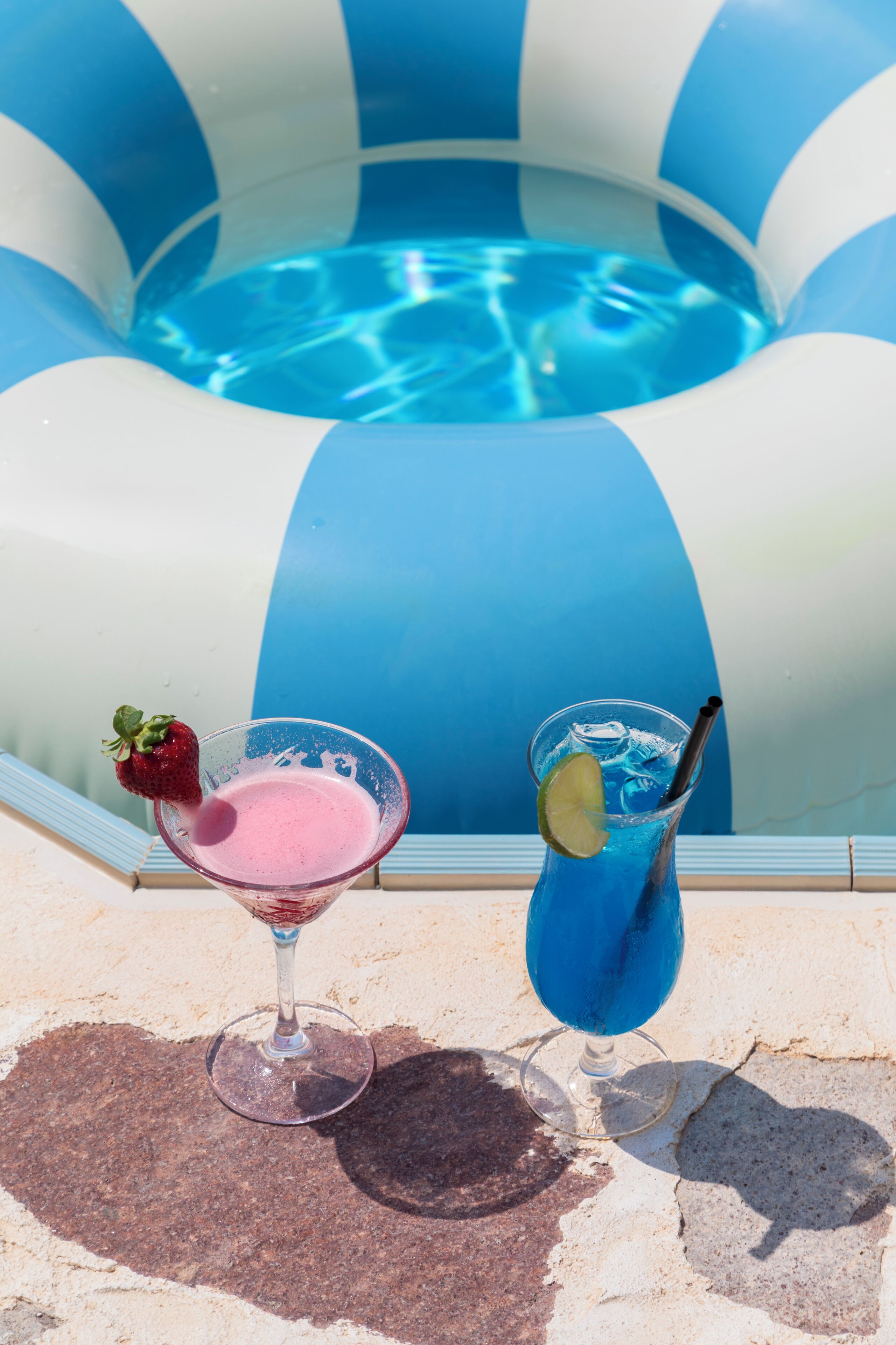 Two drinks on a stone surface with a pool in the background.
