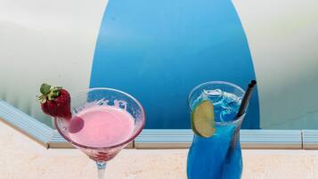 Two drinks on a stone surface with a pool in the background.