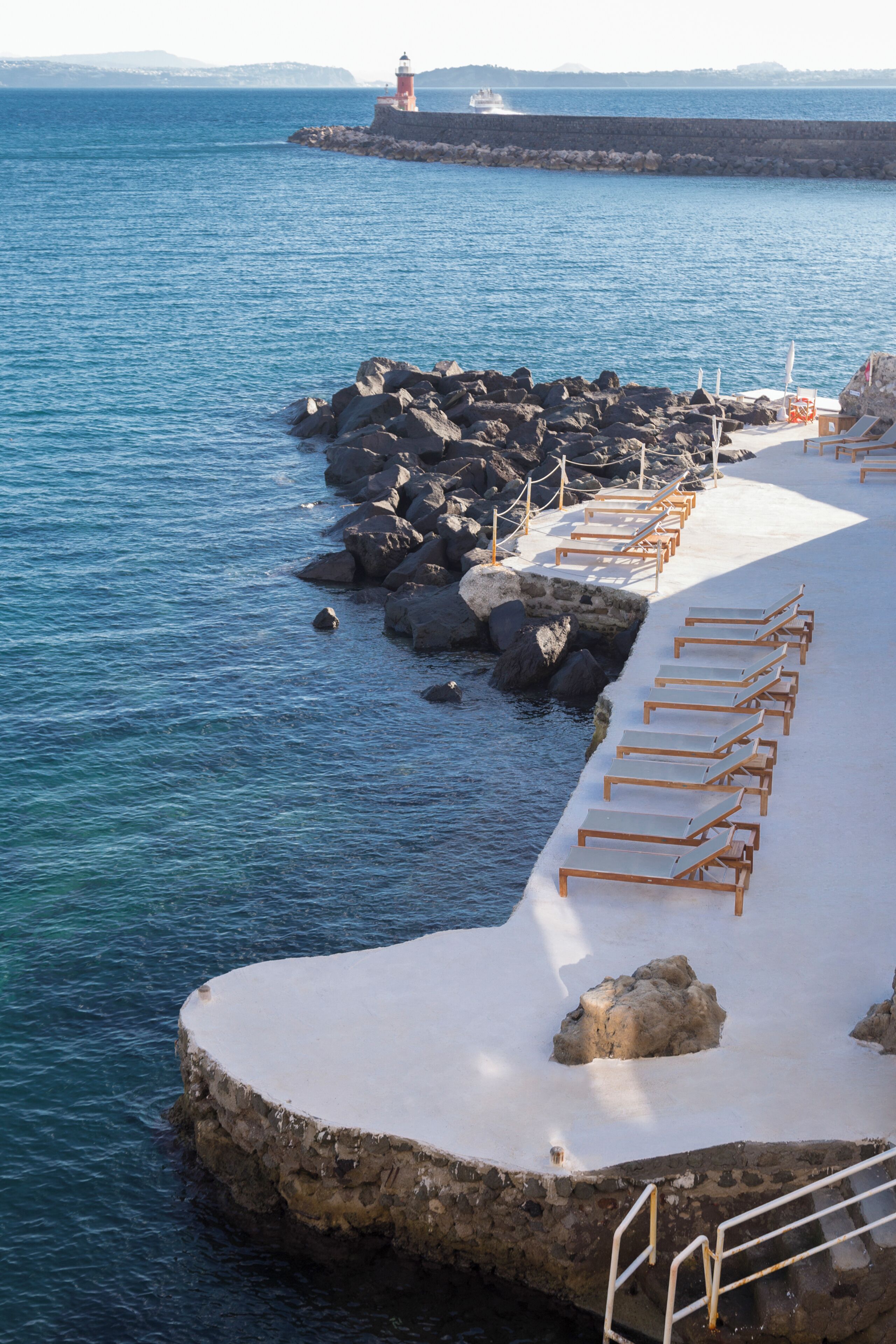 Une zone côtière avec un phare, une côte rocheuse et des chaises longues disposées sur une plateforme en béton.