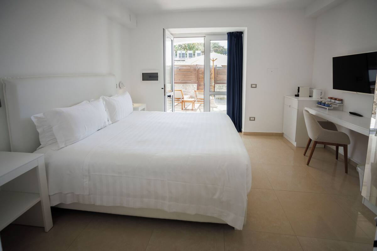 A modern hotel room with a large bed, a desk, a chair, and a TV.