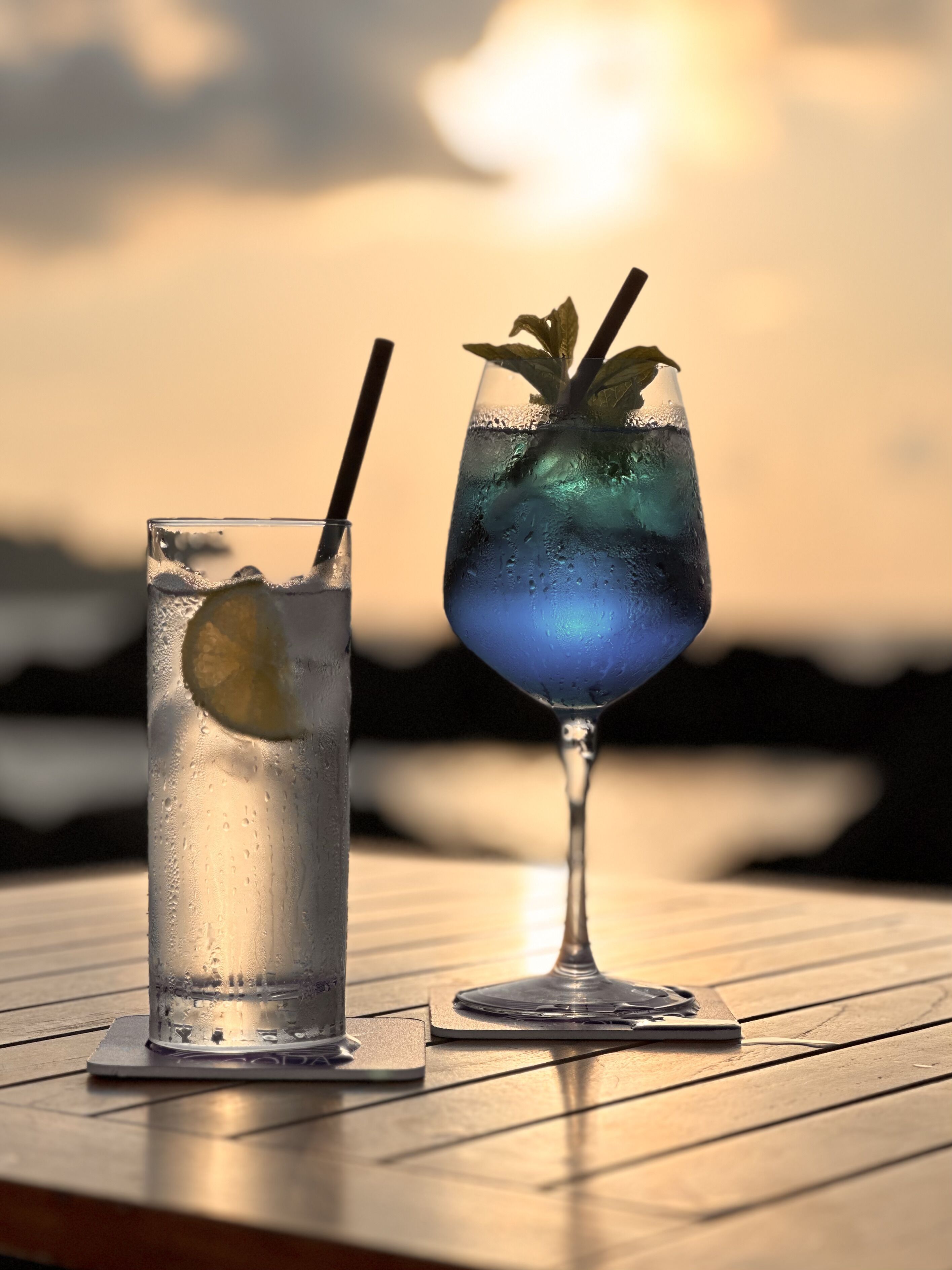 Dos vasos de bebidas heladas sobre una mesa de madera, con vistas al atardecer.