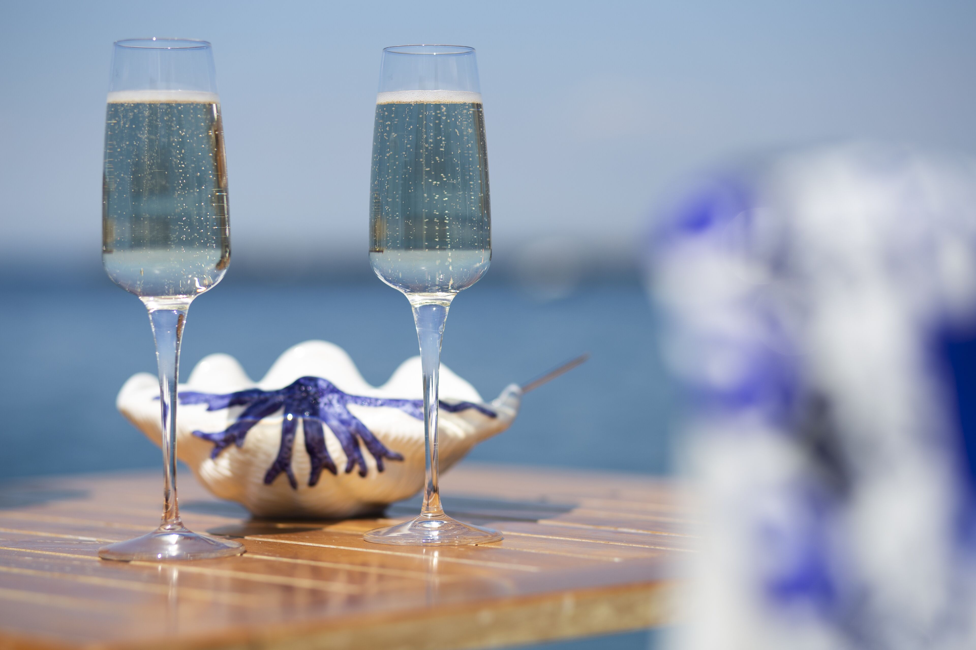 Two champagne flutes on a table with a decorative bowl in the background.