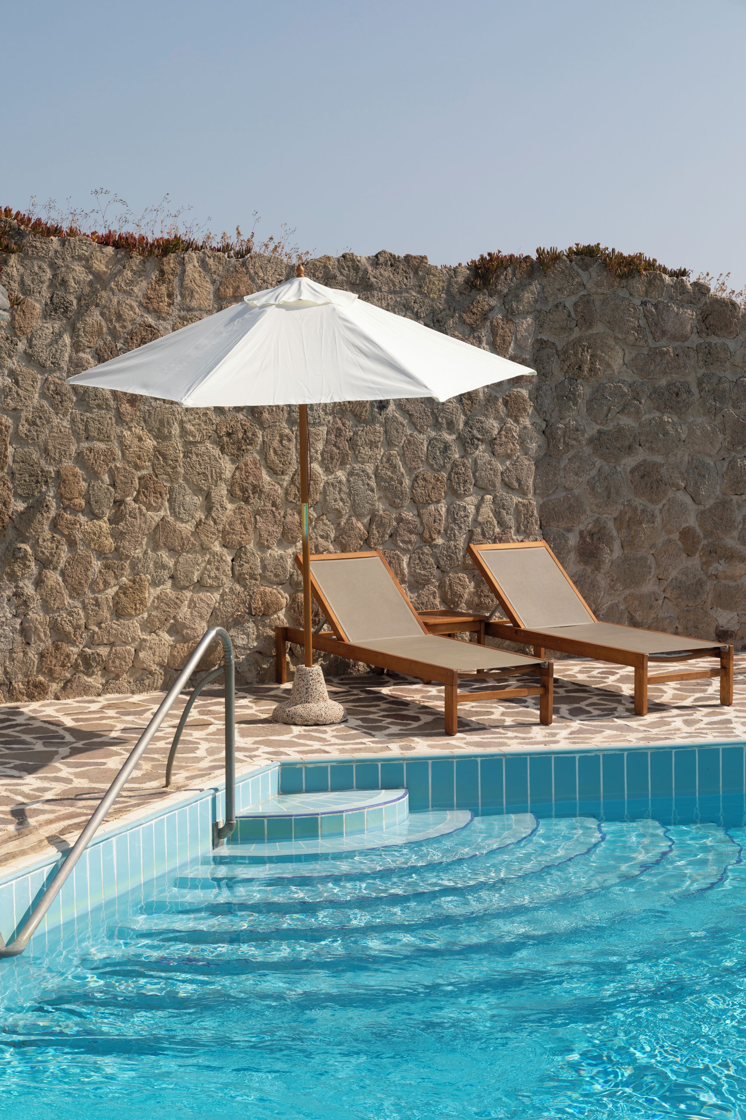 A pool area with two lounge chairs and a white umbrella.