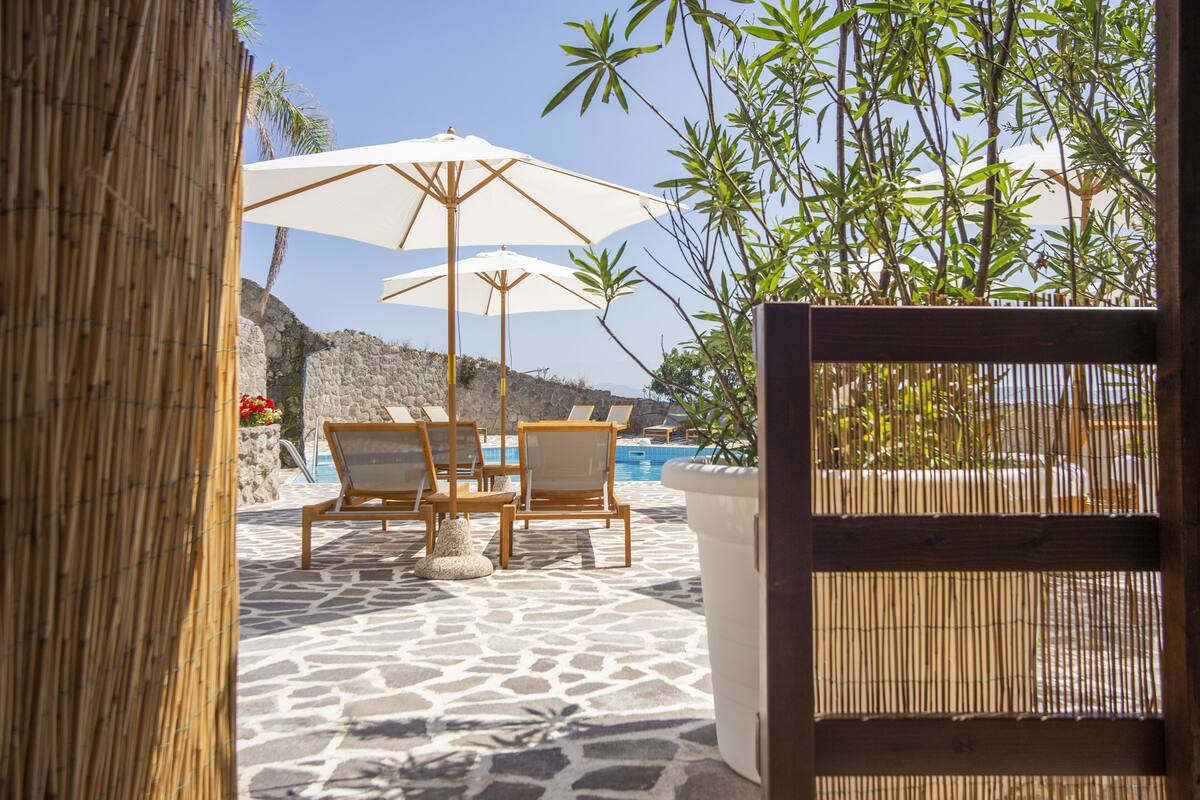 A poolside area with lounge chairs and umbrellas, surrounded by bamboo and palm trees.