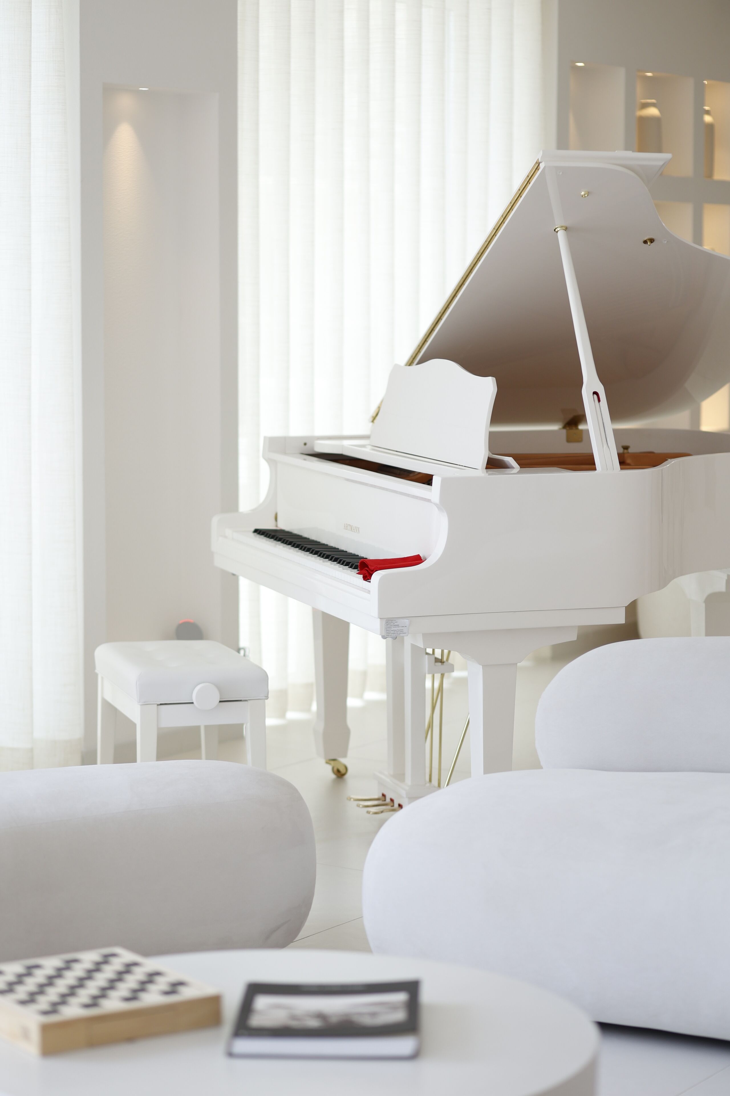 A modern living room with a white grand piano, a white sofa, and a small white table with a book and a picture frame.