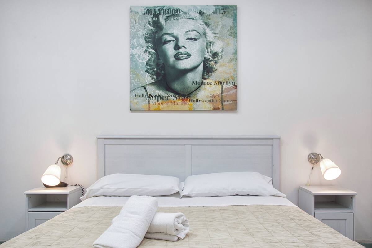 A neatly made bed with white linens, two bedside lamps, and a framed picture on the wall.