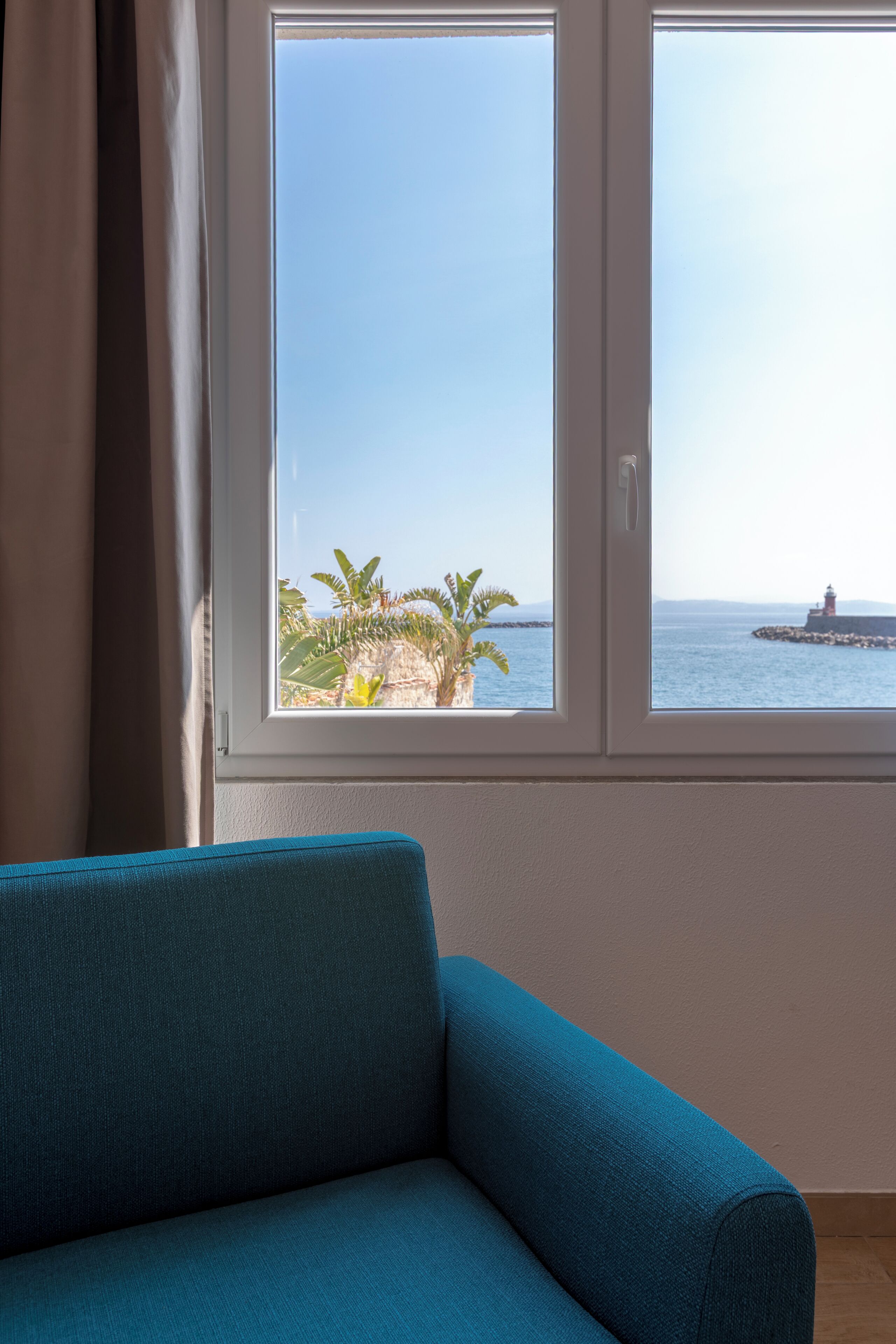 Quarto com vista para o mar, um sofá azul e uma janela com cortinas.