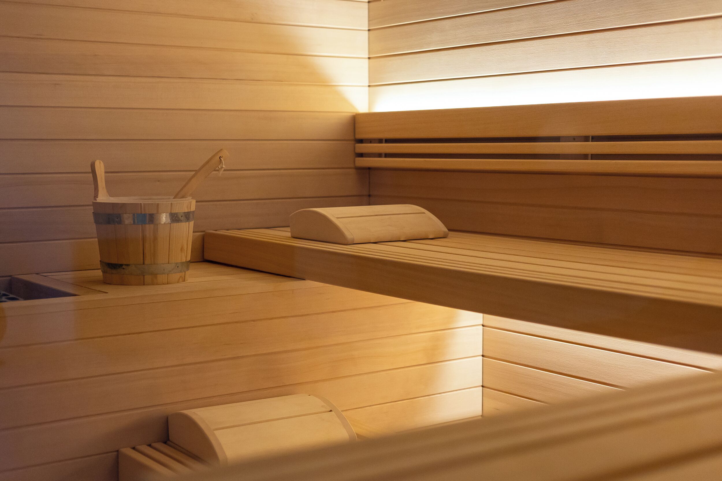 Una sauna con bancos de madera y un cubo de madera con una cuchara.
