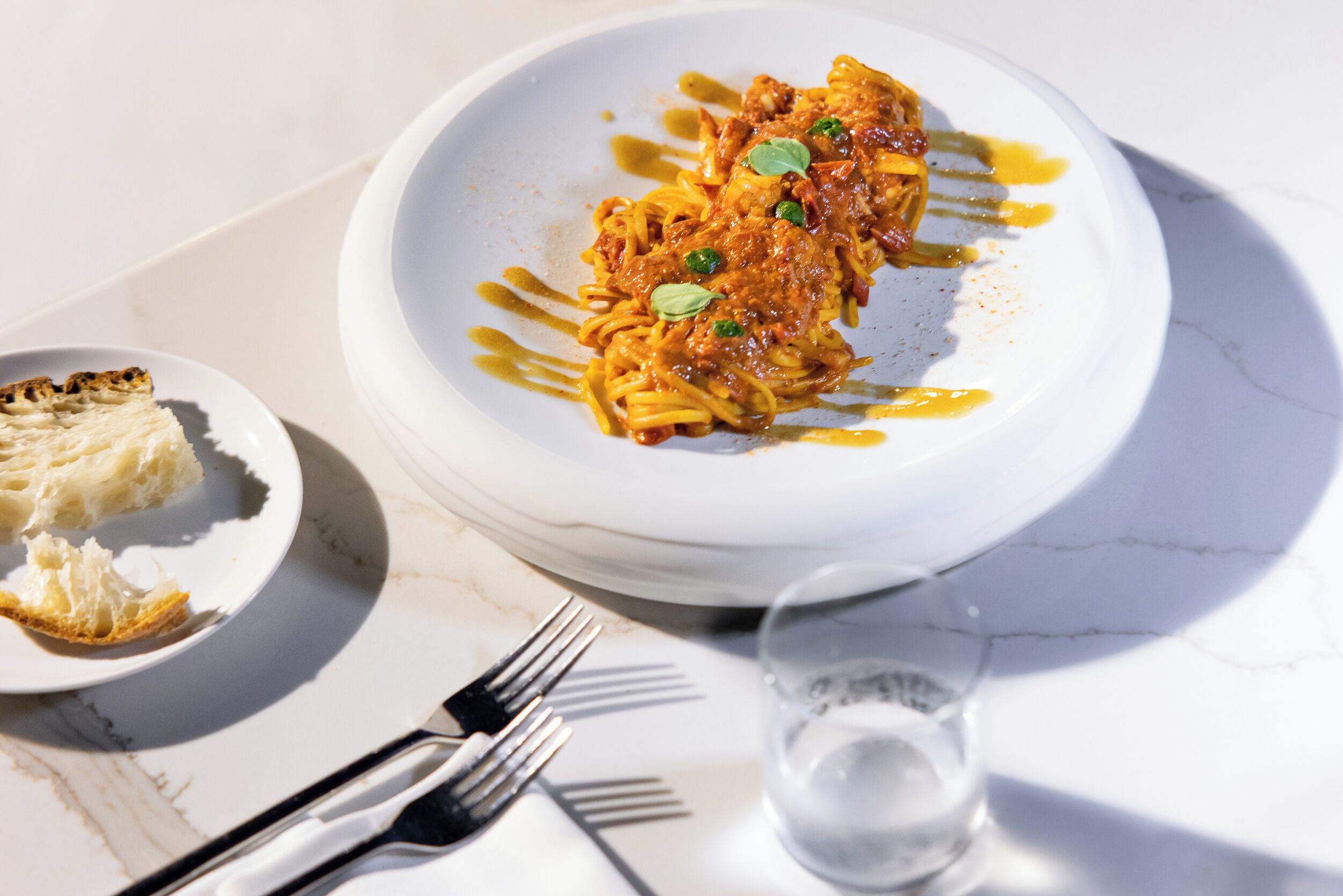 A plate of pasta with sauce, a glass of water, and a fork on a table.