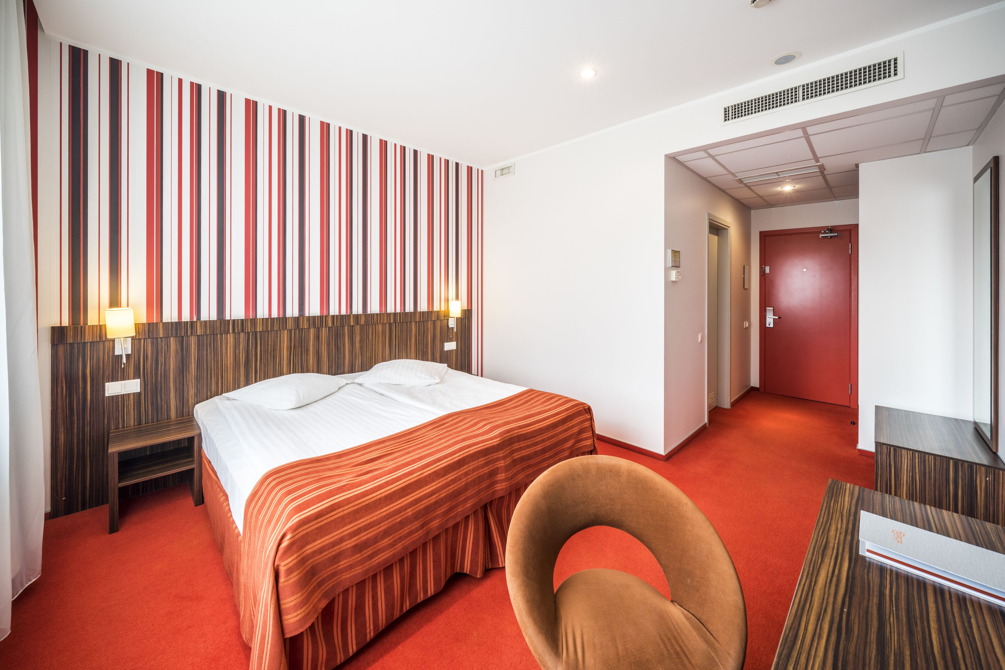 Een hotelkamer met een bed, een stoel, een bureau en een rood tapijt.