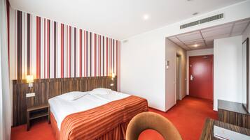 Een hotelkamer met een bed, een stoel, een bureau en een rood tapijt.