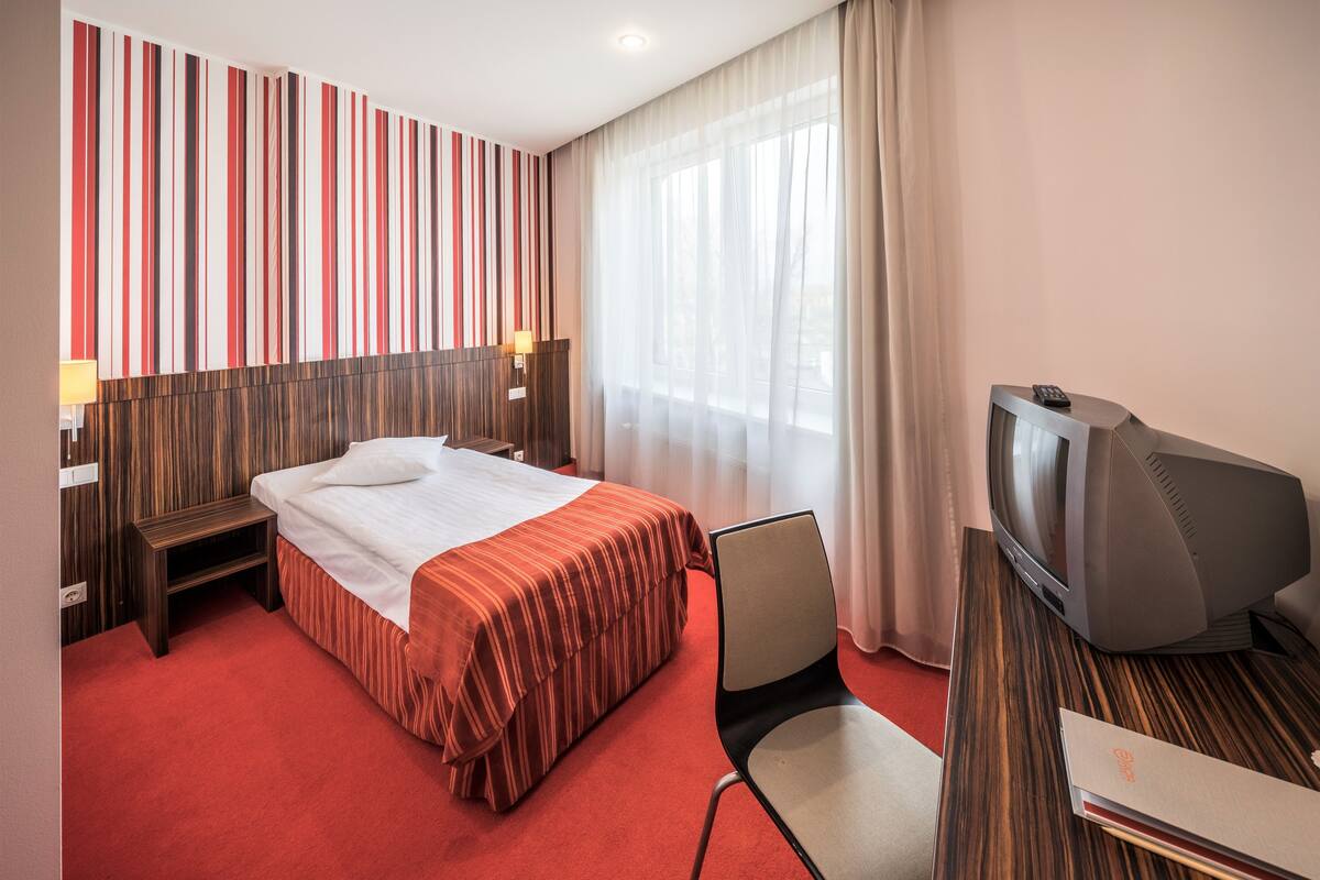 Ein Hotelzimmer mit Bett, Fernseher, Sessel und Schreibtisch.