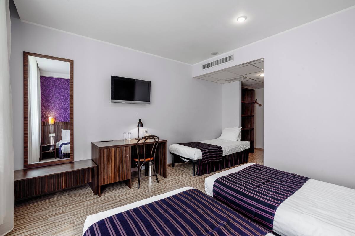 Ein Hotelzimmer mit zwei Betten, einem Schreibtisch, einem Stuhl, einem Fernseher und einem Kleiderschrank.