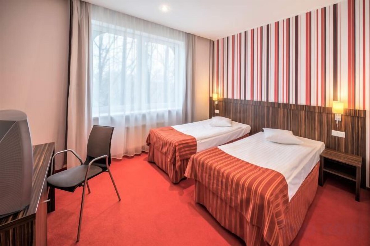 Habitación de hotel con dos camas, un escritorio, una silla, un televisor y una ventana con cortinas.