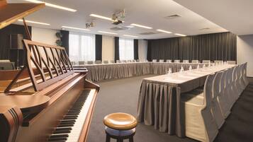 Un salón de conferencias con un piano de cola, una mesa larga con sillas y un taburete.
