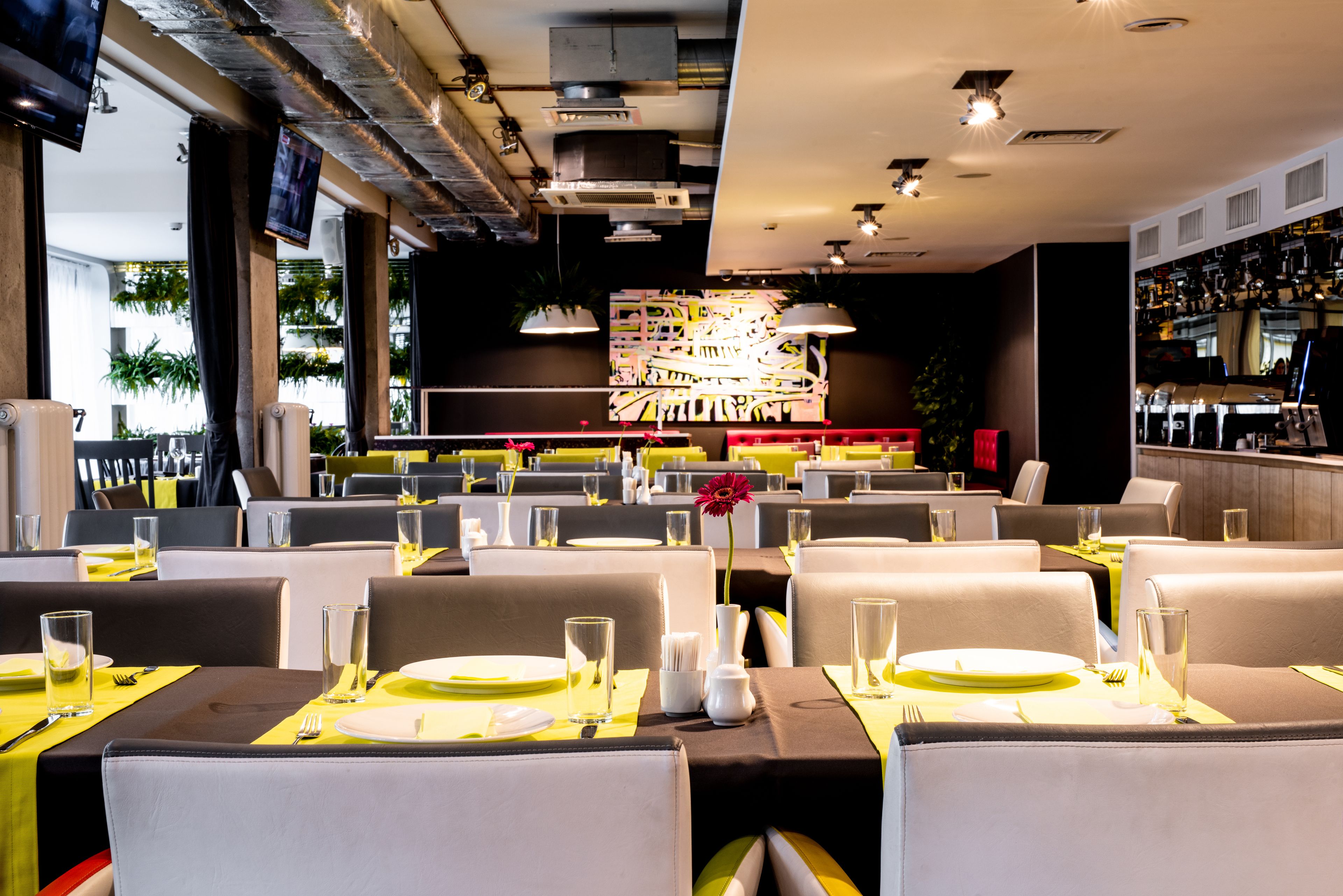 A modern restaurant with neatly arranged tables, yellow tablecloths, and a central decorative light fixture.