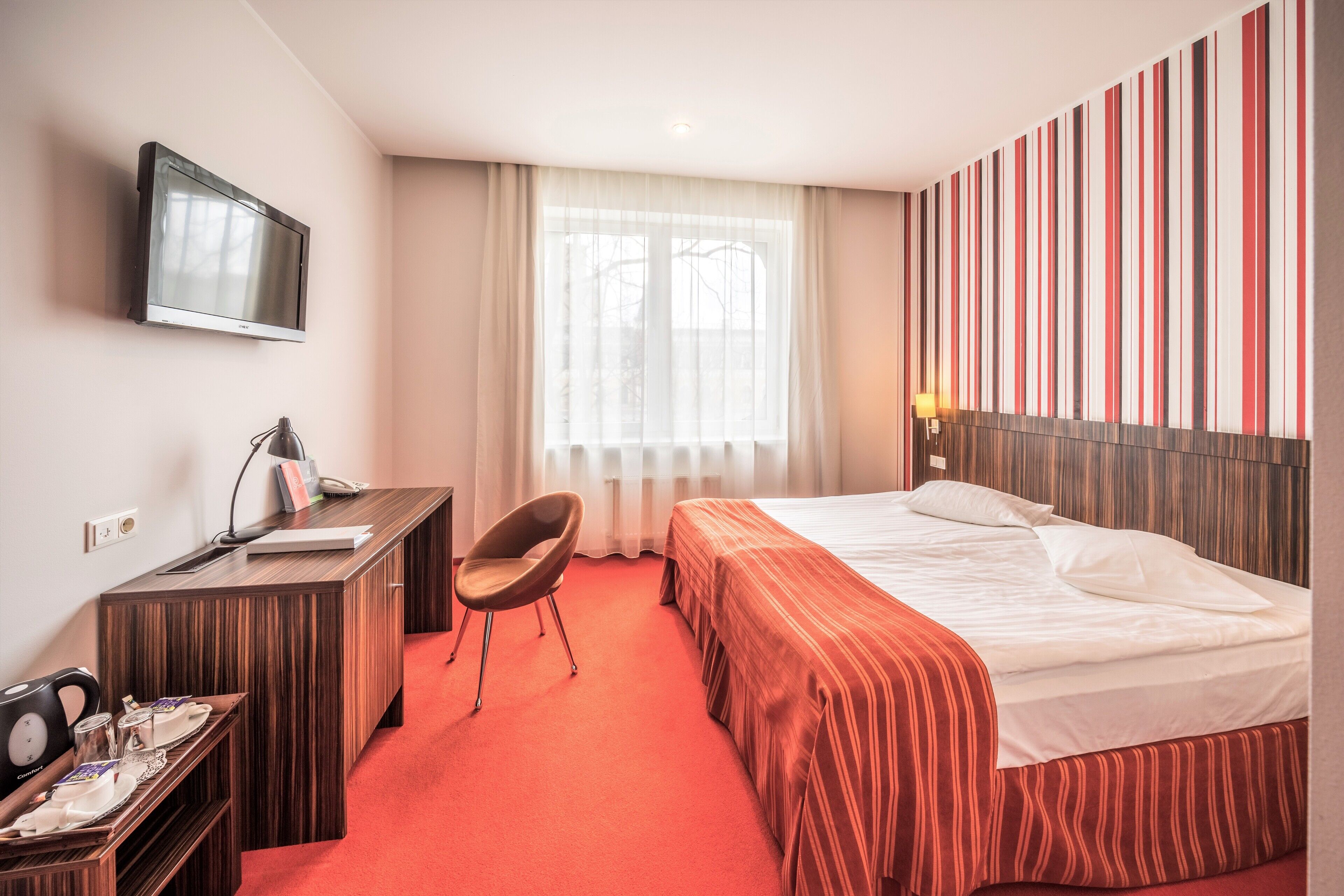A hotel room with a bed, a desk, a chair, a television, and a window with curtains.