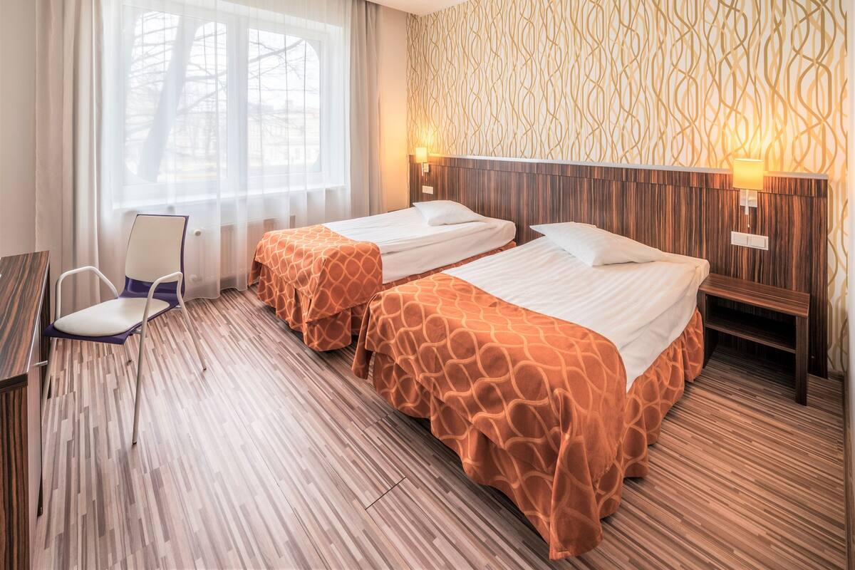 Ein Hotelzimmer mit zwei Betten, einem Schreibtisch, einem Stuhl und einem Vorhangfenster.