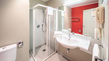 Un baño moderno con ducha de vidrio, lavamanos blanco y pared de acento roja.